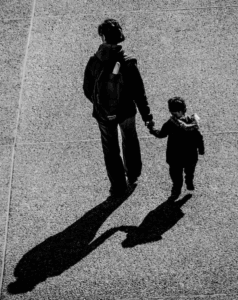 Mother and child on an open road, photographed from behind.